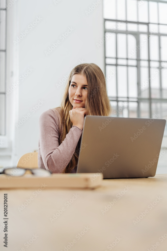 Young thoughtful woman sitting in front of laptop