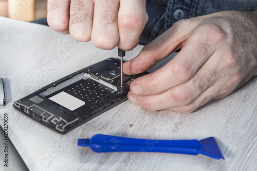 Dłonie pracownika serwisu telefonów odkręca śrubkę we wnętrzu telefonu komórkowego.