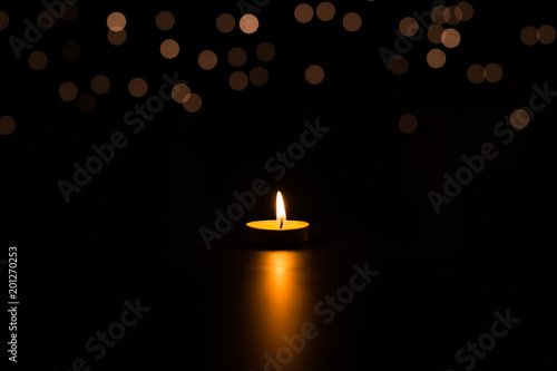 One candle in the dark with a reflection, in the background lights