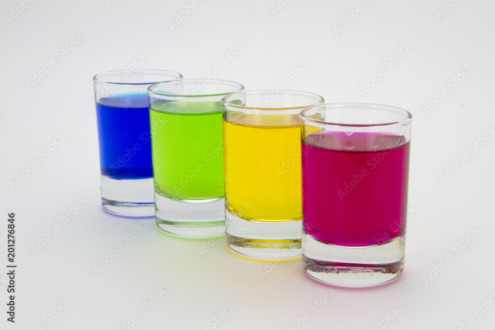 Multicolored glasses of different drinks. Party and holiday celebration concept. Four glasses with a blue, green, yellow and red drink. Isolated on white background. Multicolored glasses of different drinks. Party and holiday celebration concept. Four glasses with a blue, green, yellow and red drink. Isolated on white background.