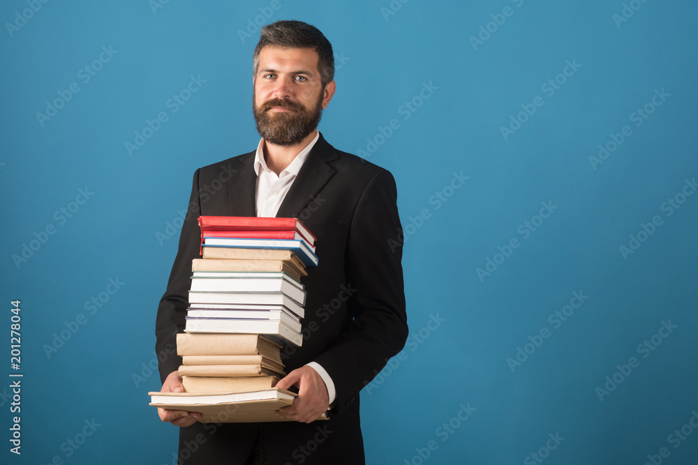 Businessman with pile of books on blue background. Literature lesson and reading book. School time of teacher in university library. Education in knowledge day. Teachers day concept, copy space Businessman with pile of books on blue background. Literature lesson and reading book. School time of teacher in university library. Education in knowledge day. Teachers day concept, copy space