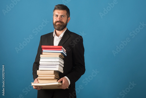 Businessman with pile of books on blue background. Literature lesson and reading book. School time of teacher in university library. Education in knowledge day. Teachers day concept, copy space