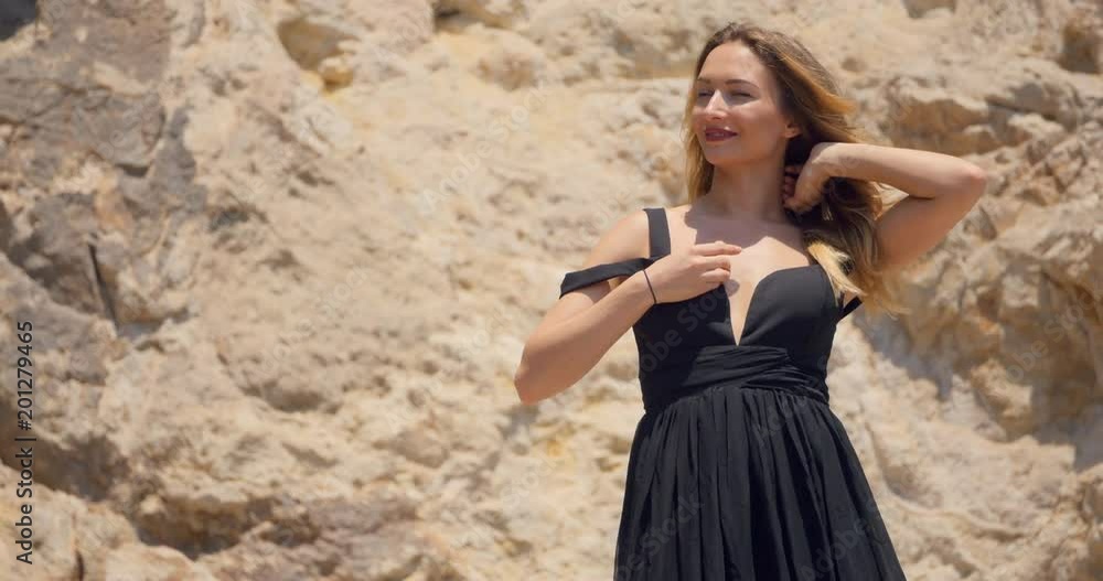 Beautiful woman with deep cutout elegant black dress on the rocks Beautiful woman with deep cutout elegant black dress on the rocks