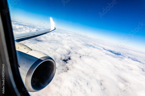On a plane, looking out of the window above the clouds, the wing is visible and the jet engine