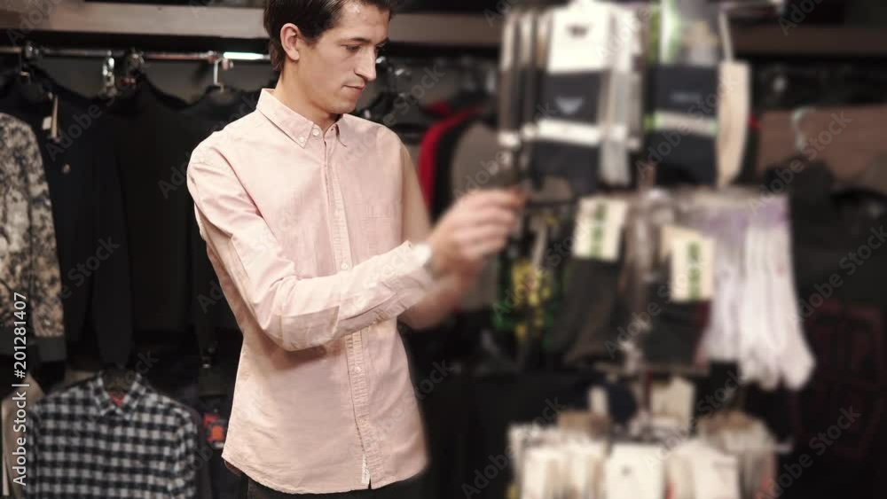 a young man examines the stand with socks, he needs to buy a gift for the clothes for the feet, the person carefully studies the composition and looks at the design on his socks a young man examines the stand with socks, he needs to buy a gift for the clothes for the feet, the person carefully studies the composition and looks at the design on his socks