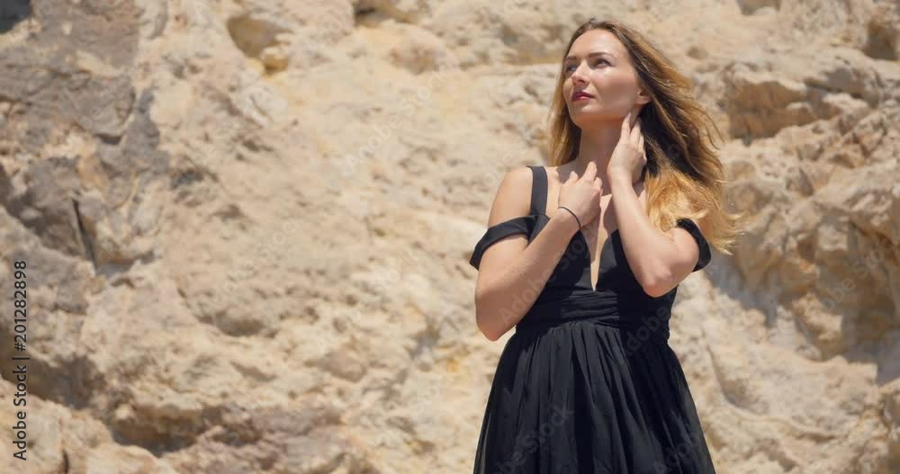 Beautiful woman with deep cutout elegant black dress on the rocks Beautiful woman with deep cutout elegant black dress on the rocks