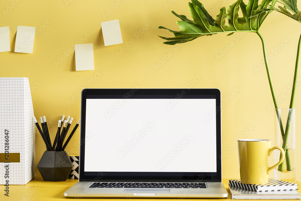 Fototapeta premium Stylish office workspace with laptop mock up screen, office accessories, leafs on the yellow wall. 