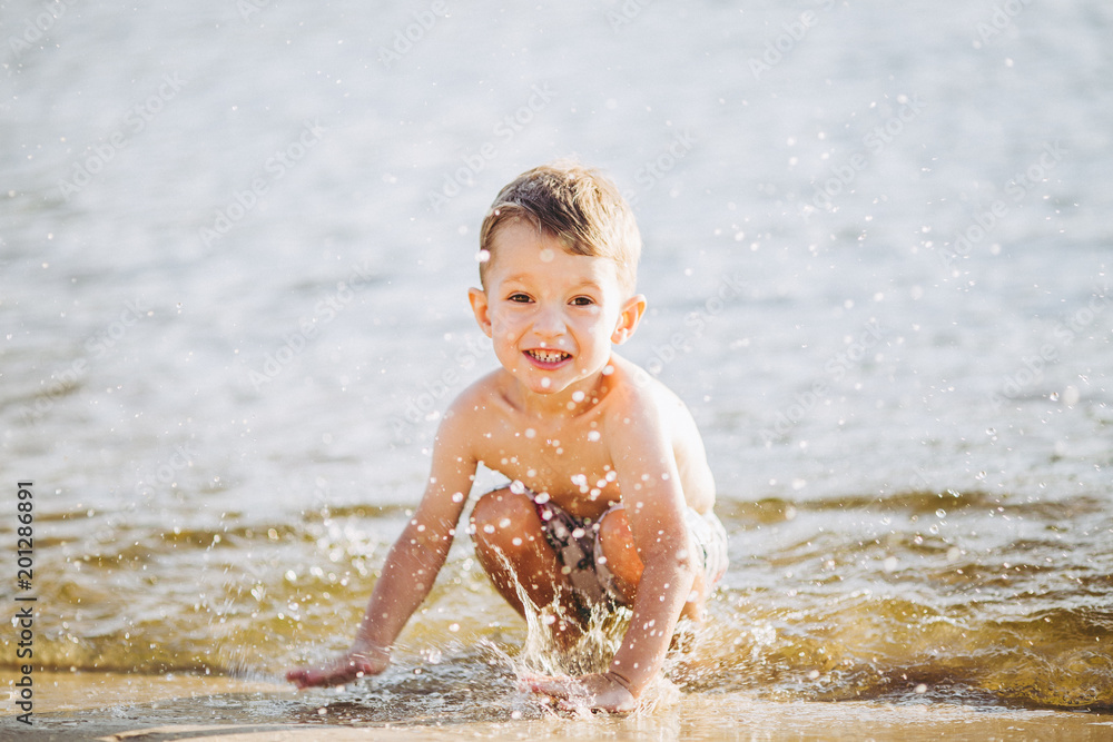 boy child playing makes splashes, beats hands on the water in the river at sunset of the day boy child playing makes splashes, beats hands on the water in the river at sunset of the day