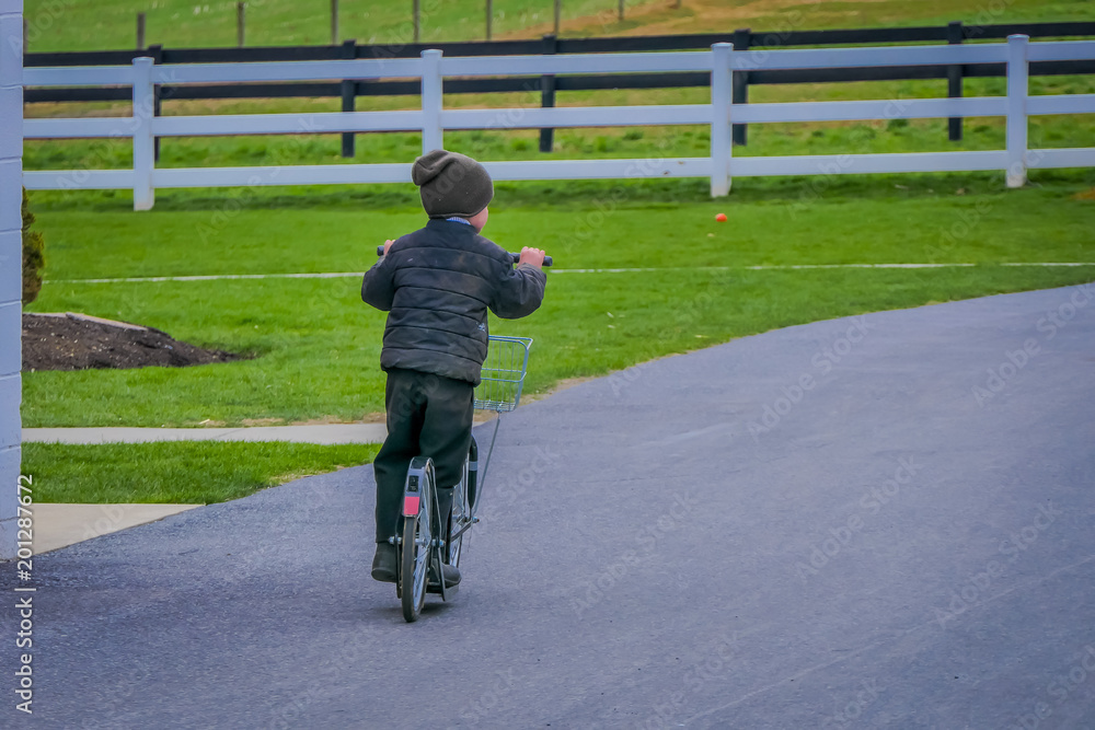 Fototapeta premium Unidentified little amish boy playing with his roller bikes or scootersin the backyard of his house