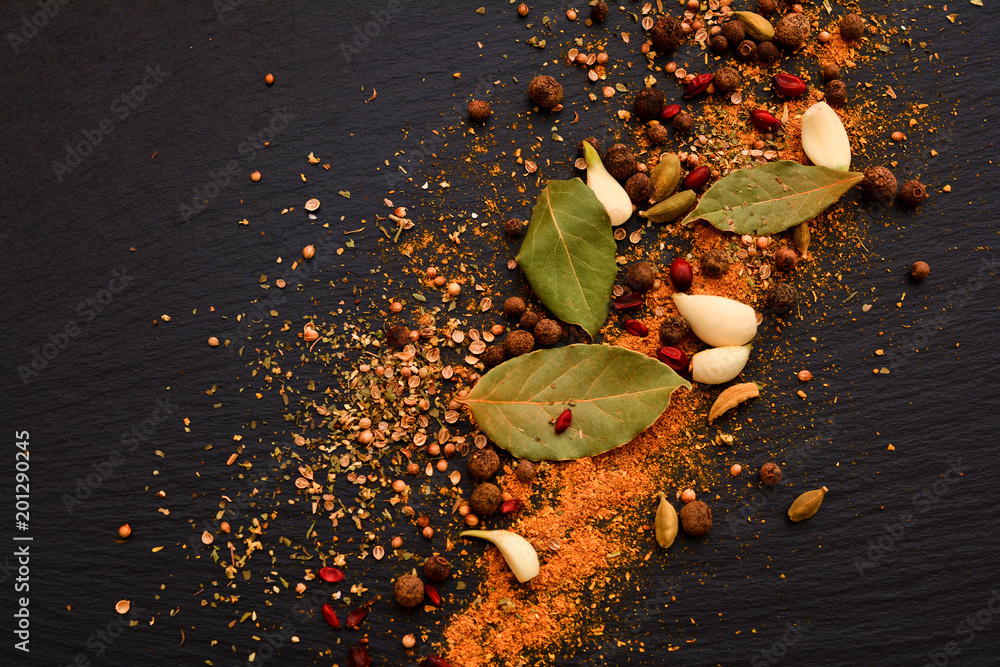 Φωτογραφία Mix of aromatic spices: black pepper, curry, cardamom, barberry, bay leaf and garlic on black slate board, plate or tray