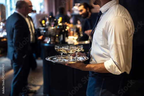 Waiter from catering service carrying champagne wine drinks on the event photo