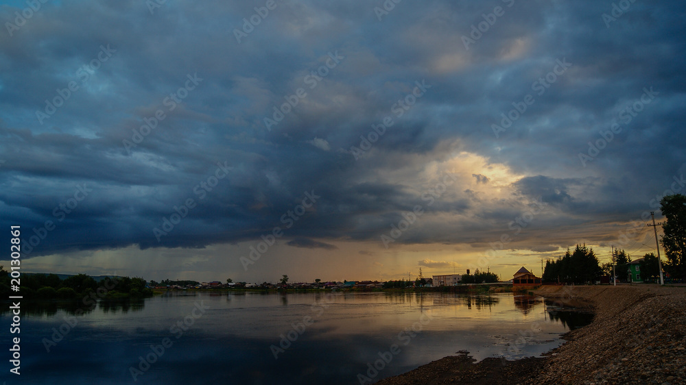 Dramatic rain clouds above the river on the sunset