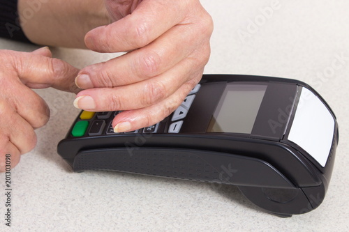 Senior woman covering hands whilst entering personal identification number on payment terminal