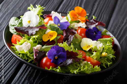 Portion of salad with edible flowers with fresh lettuce, spinach, tomatoes and cheese close-up. horizontal