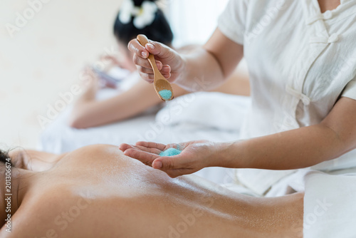 Hand of masseuse sprinkle salt down at back while young asian woman relaxing in the spa having salt scrub massage. healthy lifestyle and relaxation concept.
