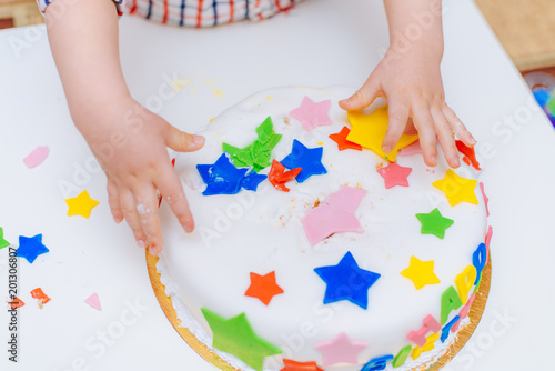 Little baby touches his birthday cake which lies on the table