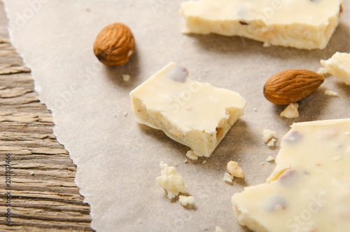White chocolate scattered on white parchment paper with nuts. Sweet dessert