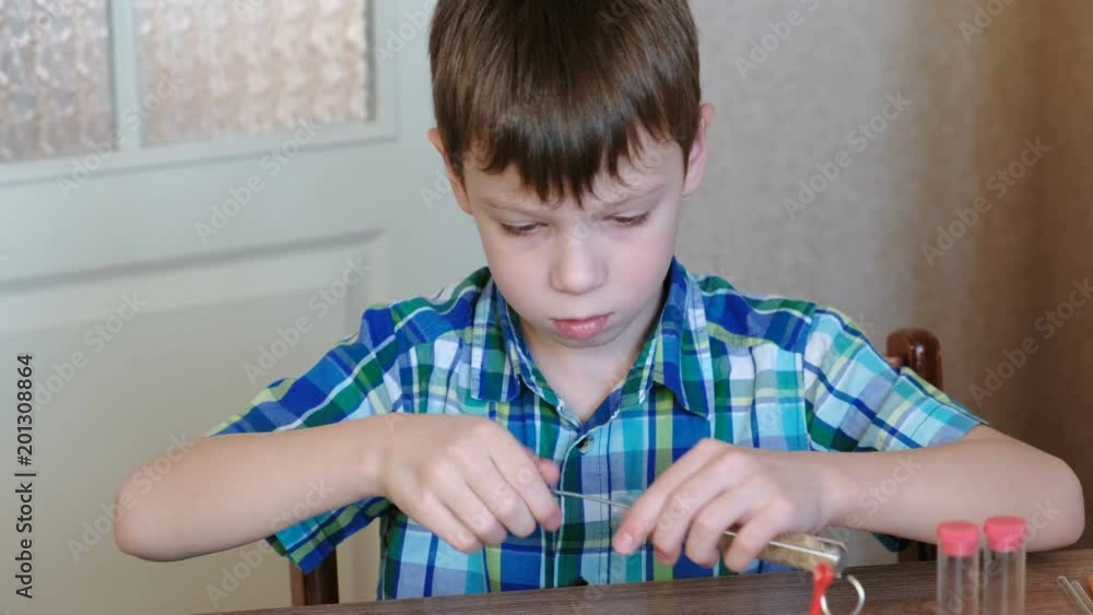 Experiments on chemistry at home. Boy in checkered shirt sits at the table and cleans the tube with a brush. Camera moving from up to bottom. Experiments on chemistry at home. Boy in checkered shirt sits at the table and cleans the tube with a brush. Camera moving from up to bottom.
