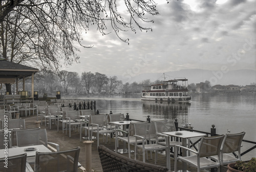 View to the lake Pamvotis. A river barge ship trasfer people to small island into the lake. Ioannina city, Greece. Vintage look processed