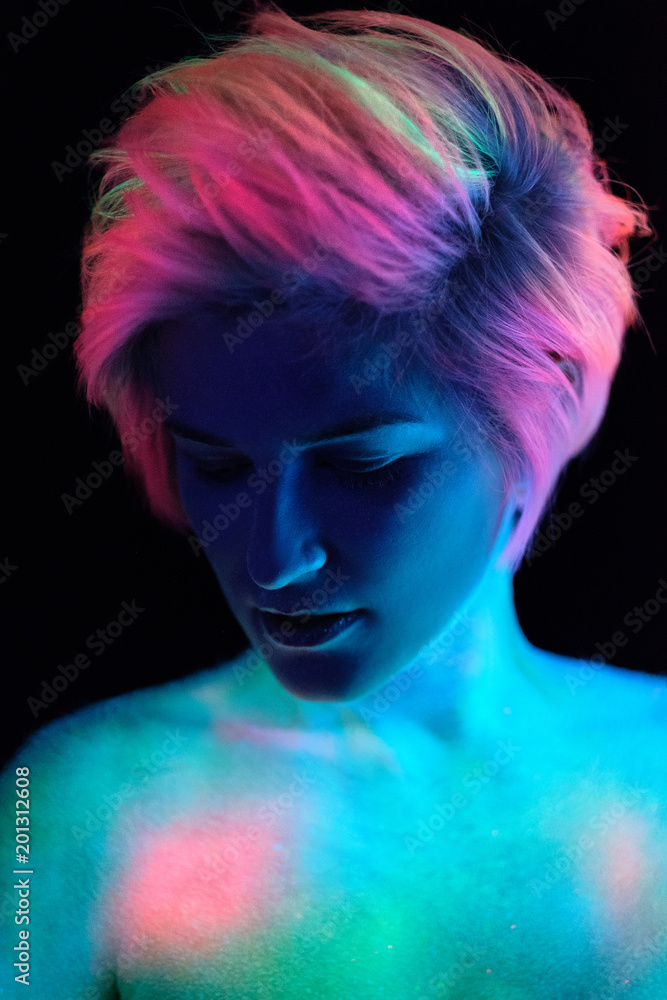 Model young beautiful girl portrait in studio with creative makeup, in neon ultraviolet lamp. Glows in the dark. Hair coloring with neon paints. Body art is blue, green, orange. Model young beautiful girl portrait in studio with creative makeup, in neon ultraviolet lamp. Glows in the dark. Hair coloring with neon paints. Body art is blue, green, orange.