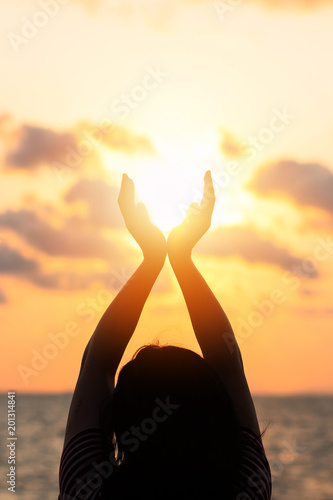 June summer sun solstice concept and silhouette of happy young woman’s hands relaxing, meditating and holding sunset against warm golden hour sky on the beach with ocean or sea background photo