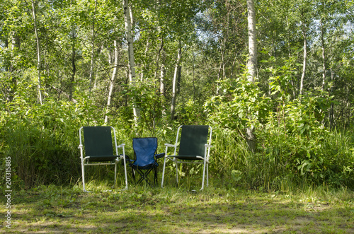 Two adult chairs and one child chair against a woodsy backdrop at a campground