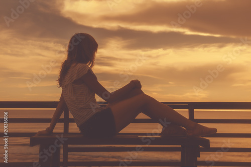 Silhoutte of a girl while sitting on a bench and looking the ocean / sea scenery.