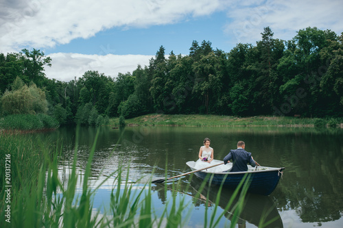 beautiful young wedding couple, blonde bride with flower and her groom just married on small boat at pond
