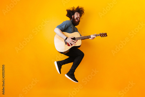 Crazy Bearded Man With Guitar Jumping Over Yellow Background photo