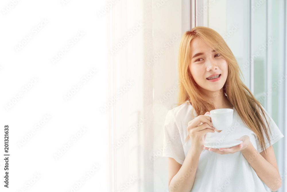 Beautiful teen standing holding coffee cup hot drink relax at the office windows with white copy space Beautiful teen standing holding coffee cup hot drink relax at the office windows with white copy space