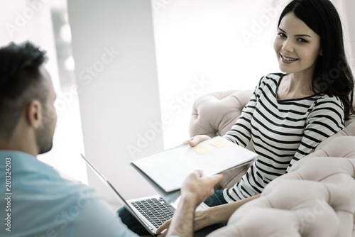One more time. Charming appealing happy woman grabbing notebook while staring at camera and smiling