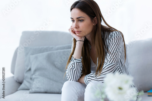 Thoughtful young woman sitting on sofa at home.