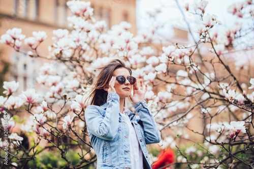 woman or pretty girl posing at blossoming tree with magnolia flowers in spring garden on sunny day
