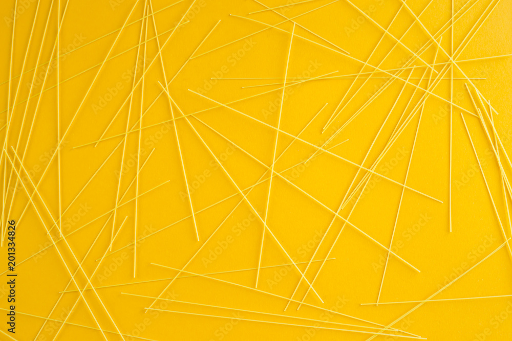 Spaghetti pasta is scattered on a yellow background. Top view, flat lay