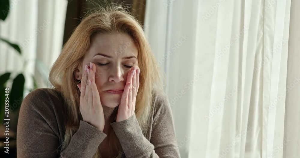 Worried middle-aged woman rocking to and fro in her chair running her hands through her long blond hair. Worried middle-aged woman rocking to and fro in her chair running her hands through her long blond hair.