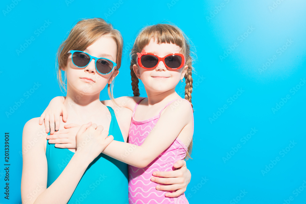 Cute girls in swimwear with glasses hugging on blue background Stock