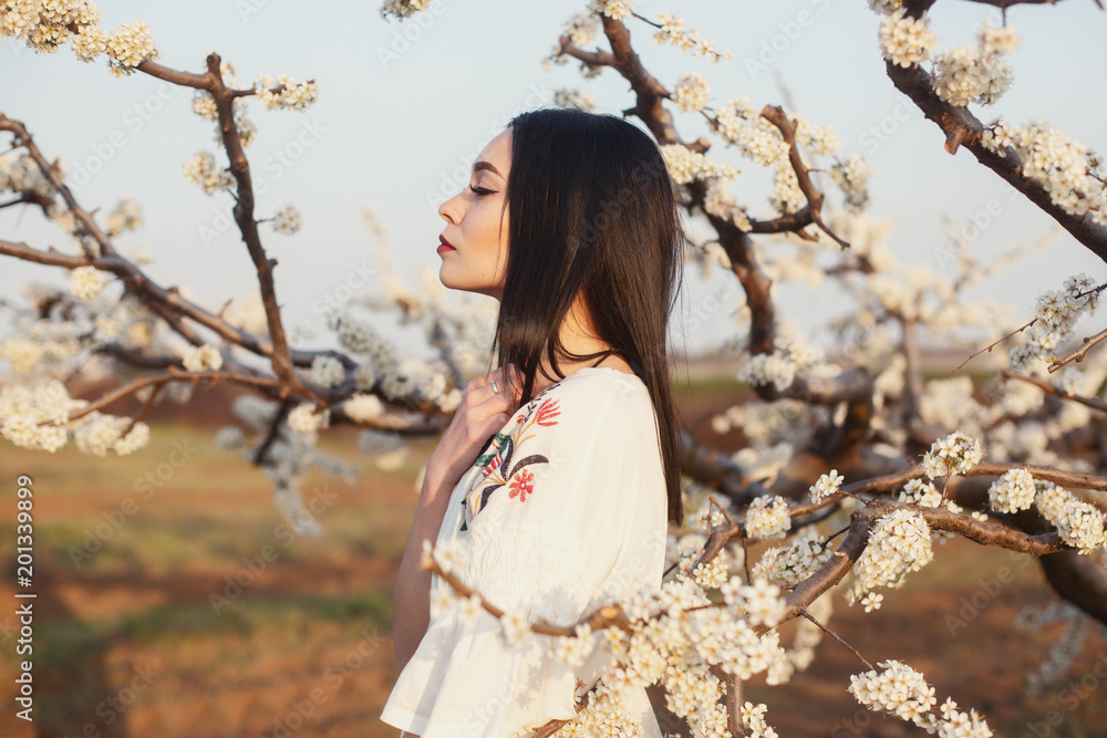 Beautiful girl with dark hair and green eyes in garden with threes and flowers Beautiful girl with dark hair and green eyes in garden with threes and flowers