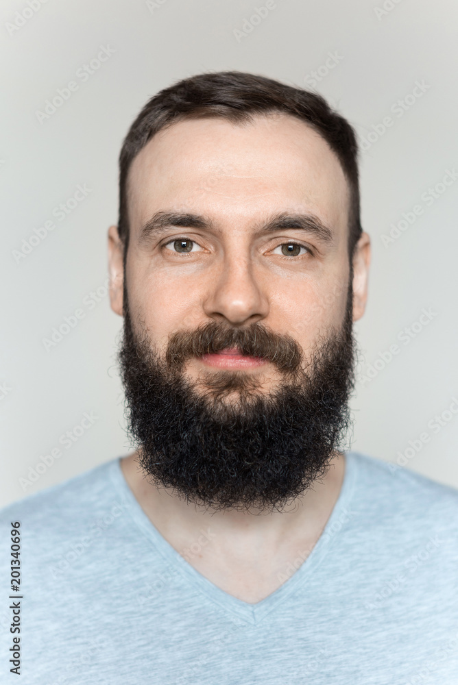Portrait of a beautiful real hipster man with a full face of a beard and mustache on a light background in a barber shop in a gray shirt Portrait of a beautiful real hipster man with a full face of a beard and mustache on a light background in a barber shop in a gray shirt