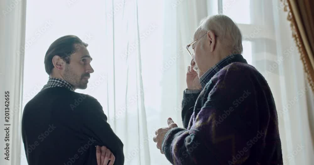 Anxious man waiting at a window staring out turning as he becomes aware of an old man behind them and then moving into an embrace of comfort. Anxious man waiting at a window staring out turning as he becomes aware of an old man behind them and then moving into an embrace of comfort.