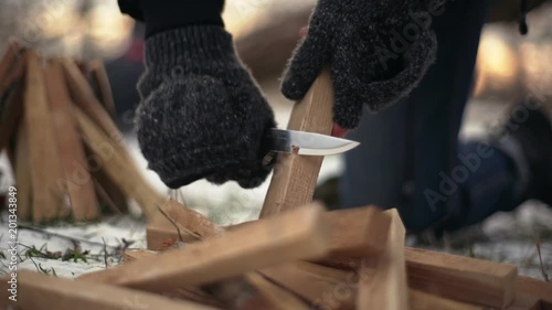 Portrait cropped of strong man in gloves cutting and whittling wooden bars with knife, outdoor on ground in winter slow motion