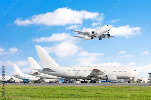 Row of passenger aircraft, airplane parked on service before departure. at the airport, other plane push back tow. One landing on the runway in the sky. © aapsky