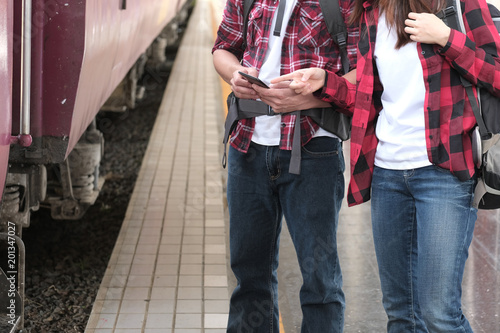 man & woman with backpack use app on smartphone at train station. traveler couple look at mobile phone. journey travel concept