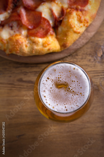 Beer and pepperoni pizza on wooden table. Glass of beer. Ale and food concept. overhead  vertical