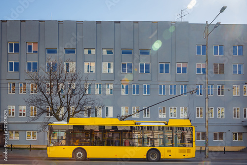 A yellow trolleybus is standing at a bus stop near the big house