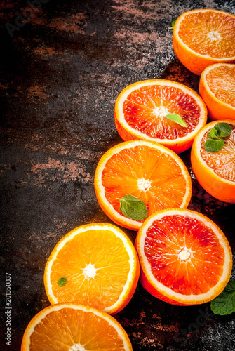 Fresh raw blood oranges, halves, with mint, on dark rusty background copy space
