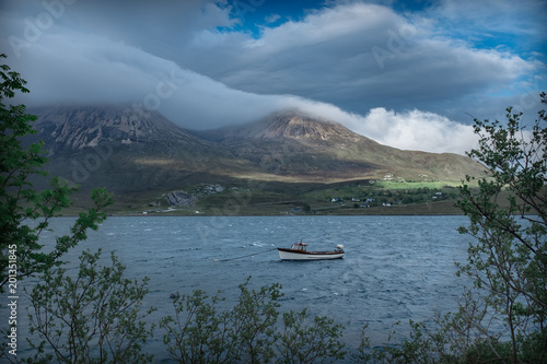 Single boat and mountains covered by clouds on a sunny day.