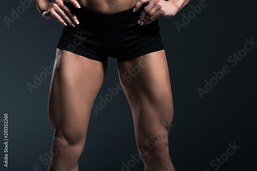 cropped view of female bodybuilders legs, isolated on grey
