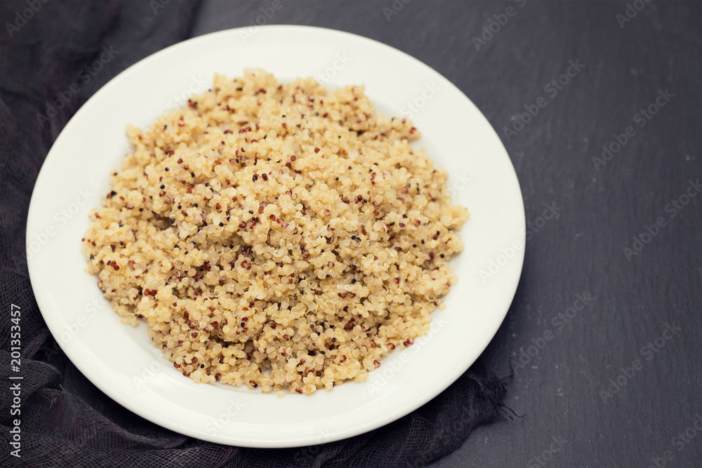 boiled quinoa on white plate on black ceramic background boiled quinoa on white plate on black ceramic background