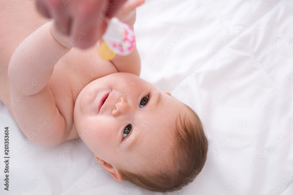 Adorable little baby girl playing with a pacifier on white bed Adorable little baby girl playing with a pacifier on white bed