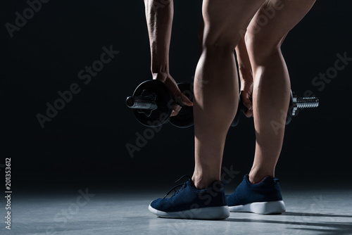 low section view of female bodybuilder in sneakers training with dumbbells  on black